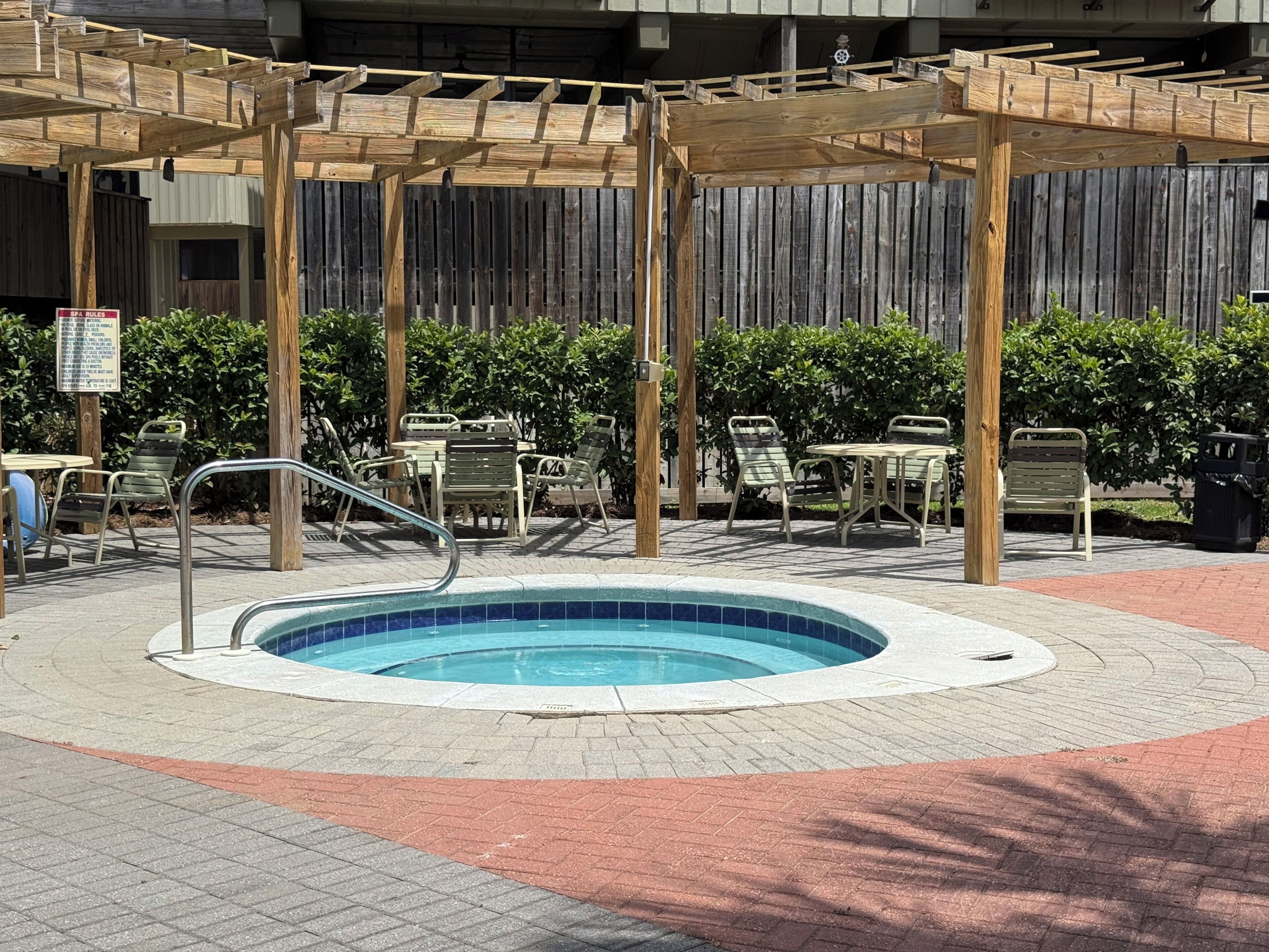 Un espace piscine agrémenté d’une pergola en bois, de sièges et d’un panneau indiquant les règles du spa.