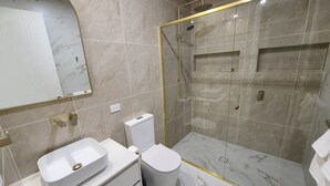 Et moderne badeværelse med et glasafskærmet brusebad, en hvid vask og et toilet.