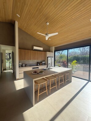 A modern kitchen with a large island, wooden ceiling, and large windows. - Casa Solana: 4BR retreat, pool, walk to beaches & surf in Playa Avellanas (Guanacaste Province)