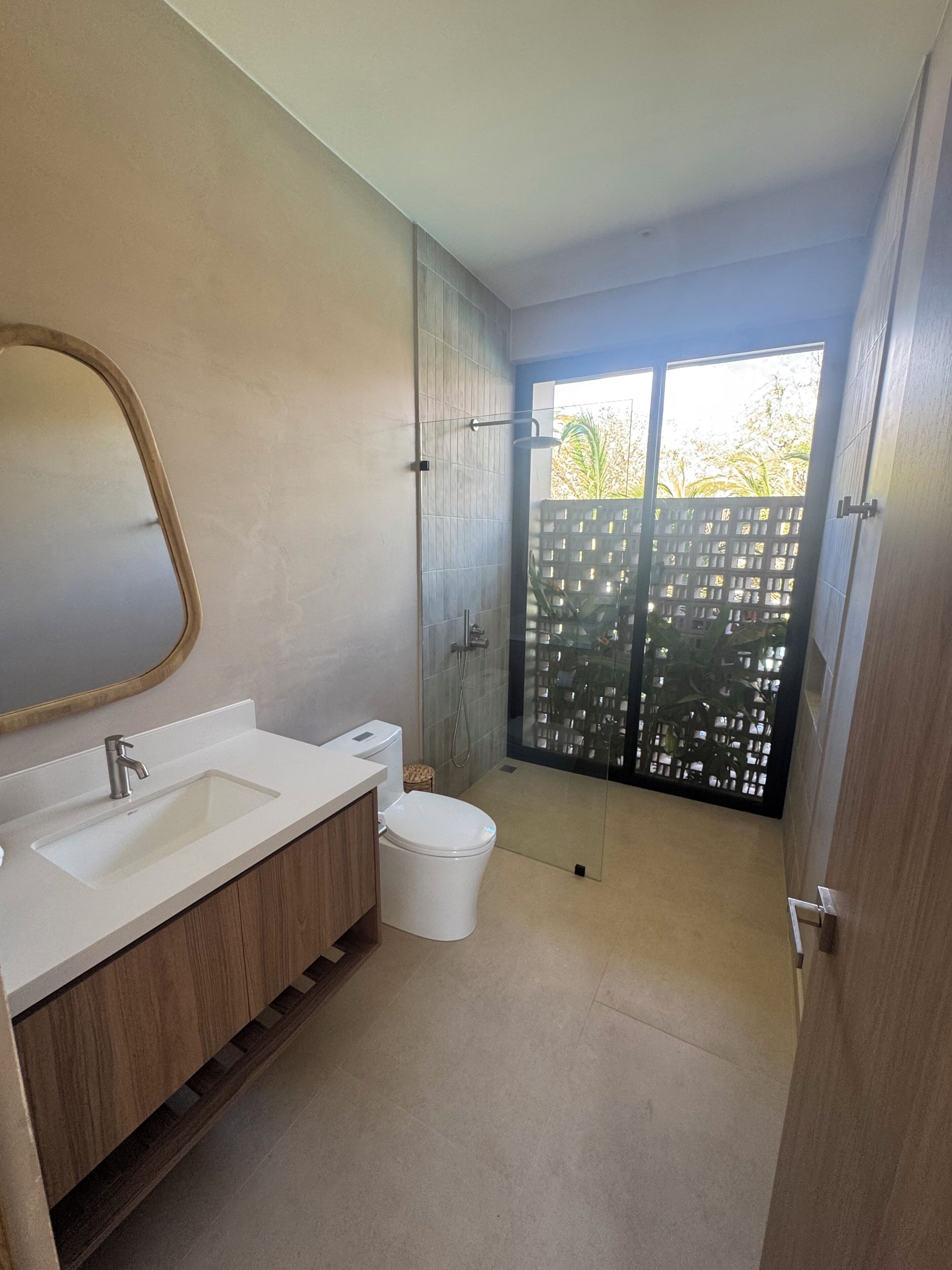 A modern bathroom with a large mirror, two sinks, a toilet, and a shower area.