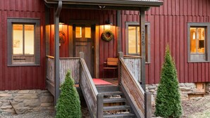 A red wooden building with a porch, a stone foundation, and a small Christmas tree. - 10 min to Asheville | Creekside, Fire Table, Games (Asheville)