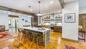 A spacious kitchen with a large island, bar stools, pendant lighting, and wooden flooring. - 10 min to Asheville | Creekside, Fire Table, Games (Asheville)