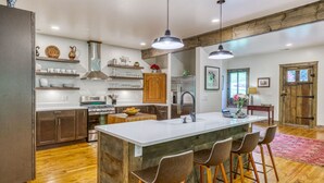 A modern kitchen with a large island, bar stools, wooden cabinets, and a farmhouse-style door. - 10 min to Asheville | Creekside, Fire Table, Games (Asheville)