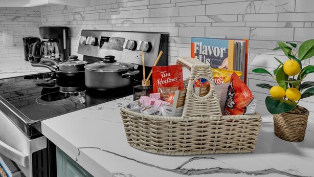 A kitchen with a stove, pots, a coffee maker, a wicker basket with food items, and a potted lemon plant.