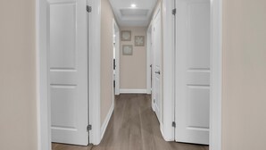 A hallway with white doors, a light-colored wall, and a wooden floor.