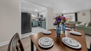 A dining area with a table set for four, a vase with flowers, and a kitchen in the background.