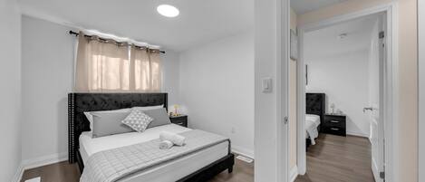 Un dormitorio con cama, mesitas de noche, un espejo y una puerta que da a otra habitación.