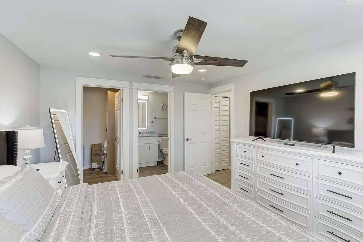 A bedroom with a bed, a dresser, a TV, a ceiling fan, and a bathroom visible through an open door.