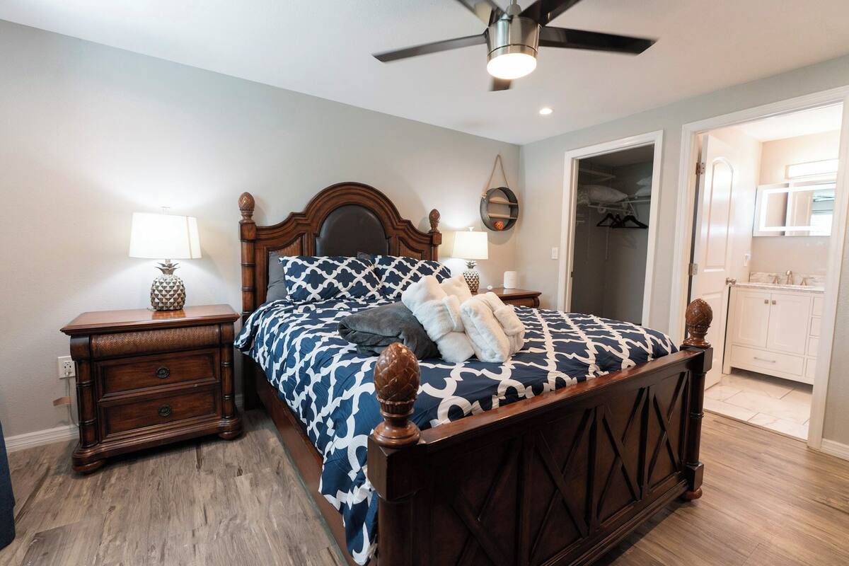 A bedroom with a wooden bed, two bedside tables, a ceiling fan, a mirror, and a walk-in closet.