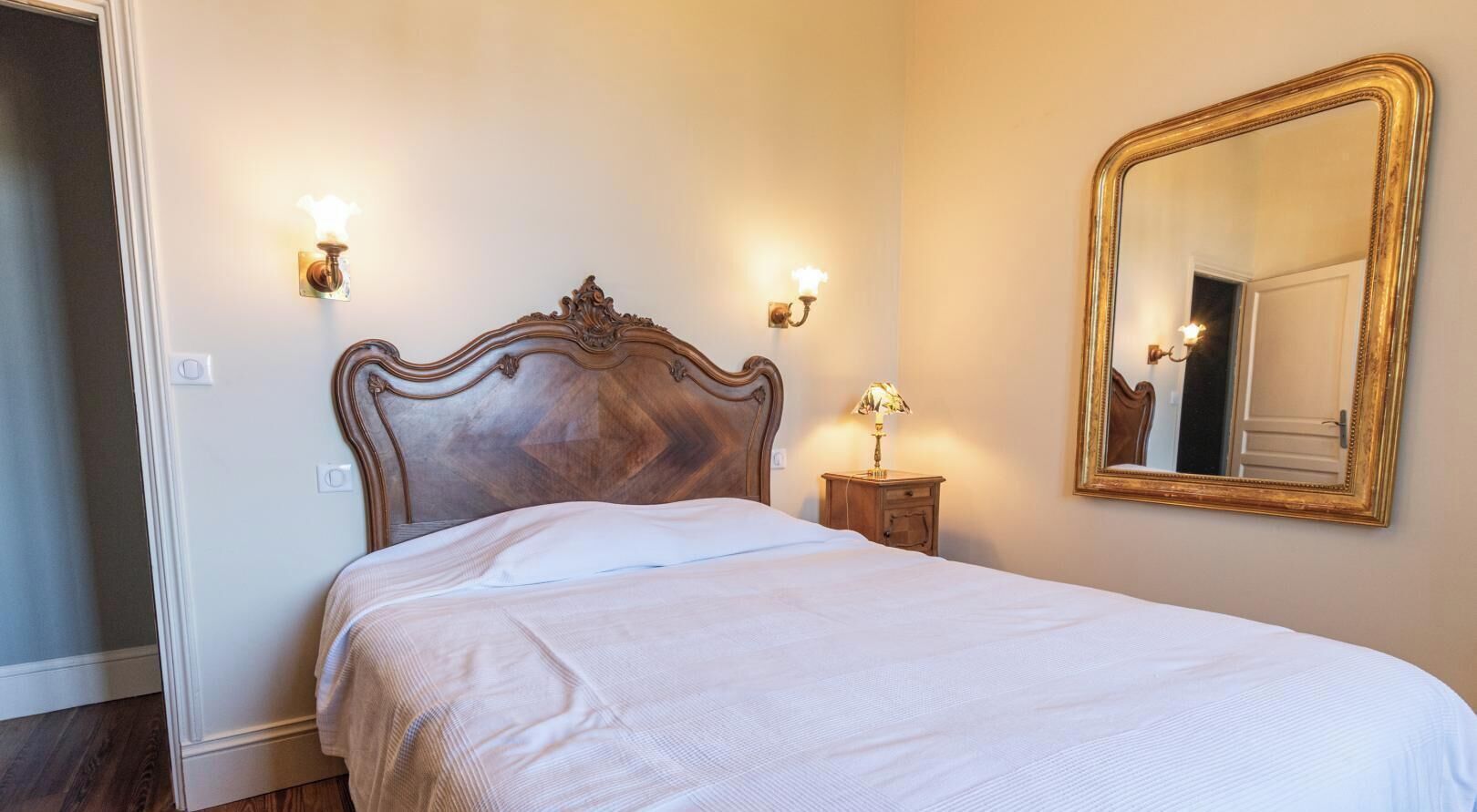 A bedroom with a wooden headboard, a large mirror, and bedside lamps.