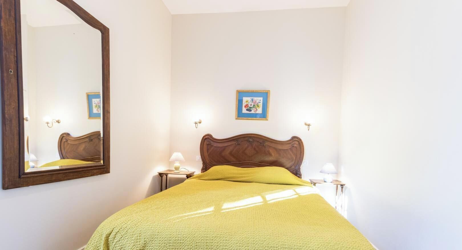 A bedroom with a bed, a mirror, two bedside tables, and a wall-mounted picture.