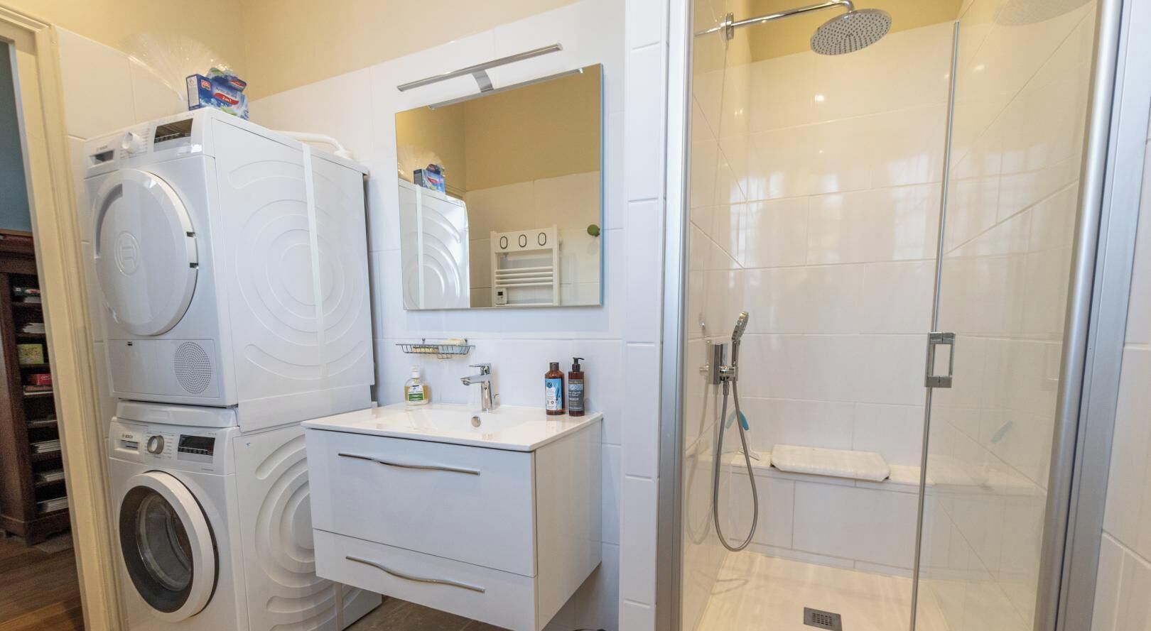 Een badkamer met een wasmachine, een wastafel, een spiegel en een douche.
