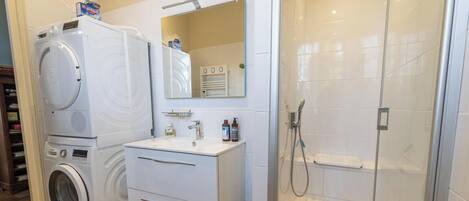 Een badkamer met een wasmachine, een wastafel, een spiegel en een douche.