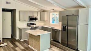 Een moderne keuken met een centraal eiland, roestvrijstalen apparatuur en een raam dat voor natuurlijk licht zorgt.