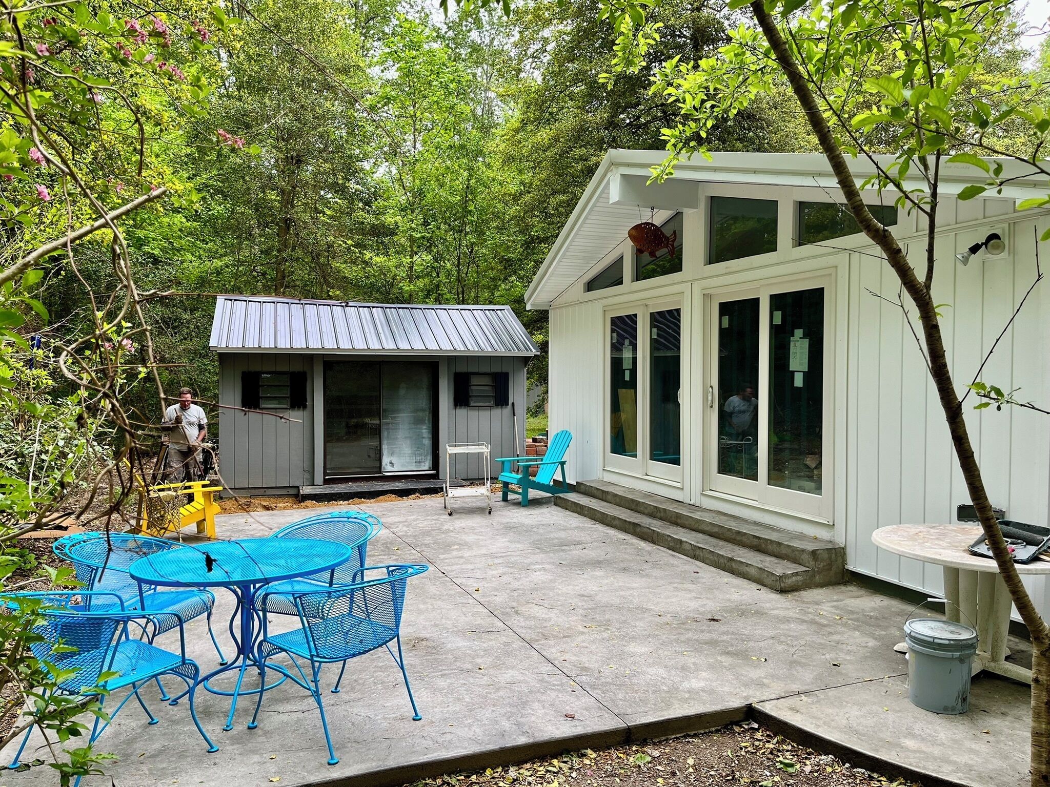 Ein Terrassenbereich mit Tisch und Stühlen, eine kleine Gartenhütte und ein überdachter Bereich mit großen Fenstern.