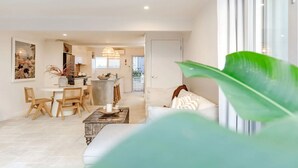 En moderne stue med sofa, spisebord og stole. Der er et køkkenområde i baggrunden med udsigt udad.