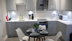 Et moderne køkken med lysegrå skabe, et spisebord dækket med skåle og glas, og en indbygget ovn.