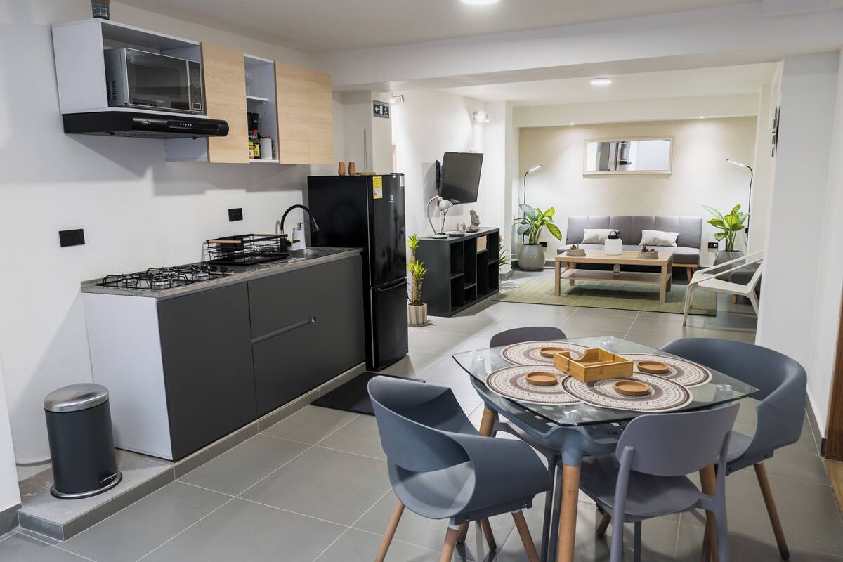 A modern kitchen with a gas stove, black refrigerator, microwave, and a dining area with a glass table and chairs.
