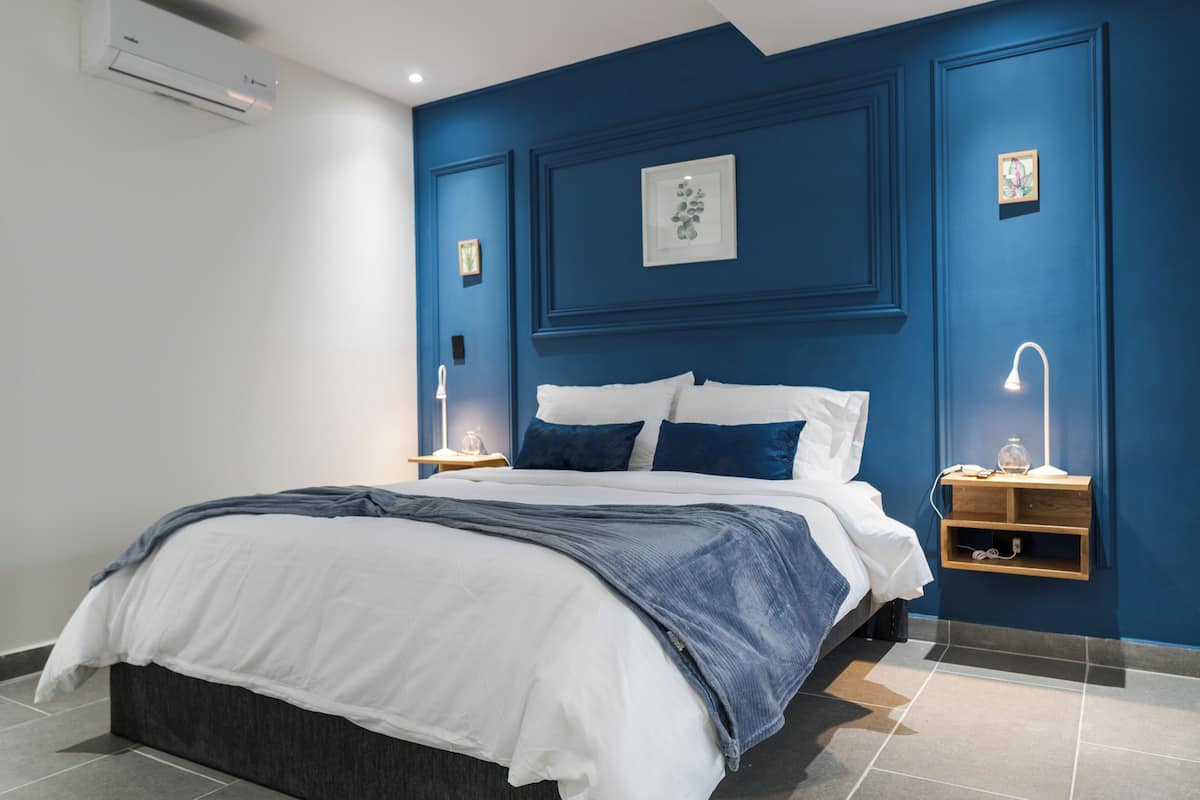 A modern bedroom with a large bed, a nightstand, a wall-mounted shelf, and a ceiling air conditioner.