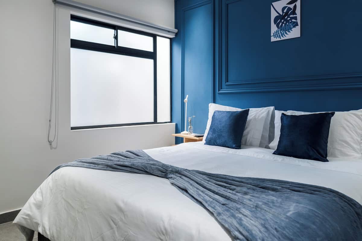 A bedroom with a large bed, a nightstand, a window, and a blue accent wall.