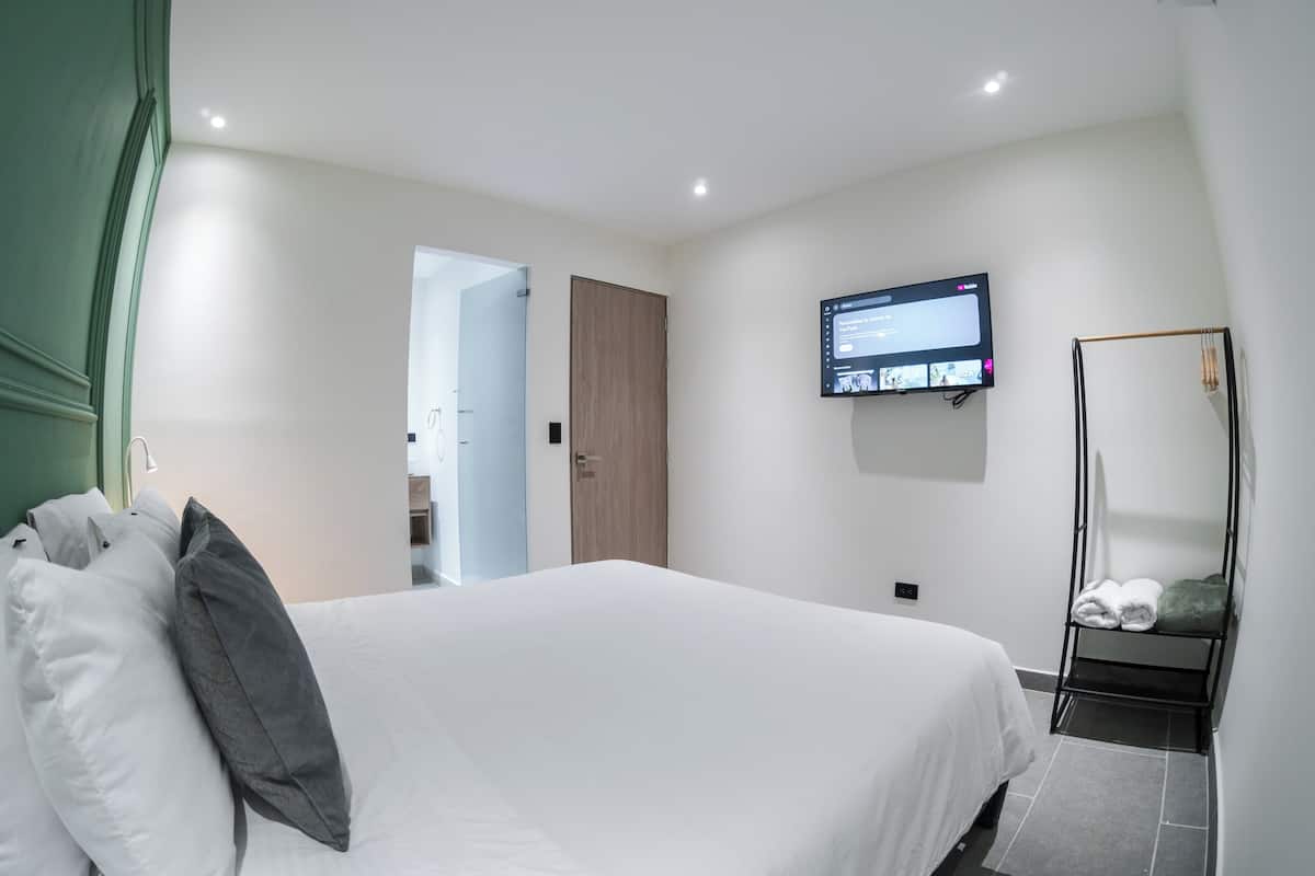A hotel room with a bed, a television mounted on the wall, and a mirror.