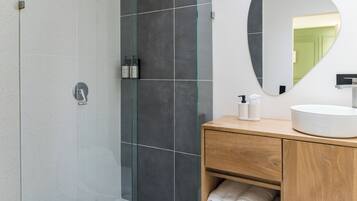 Un bagno moderno con cabina doccia in vetro, un mobile bagno in legno con lavandino e uno specchio sopra il mobile.