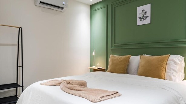 A neatly made bed with pillows, a bedside table with a lamp, and a wall-mounted air conditioner. - Fresco Provenza Living - Musical lifestyle (Medellín)