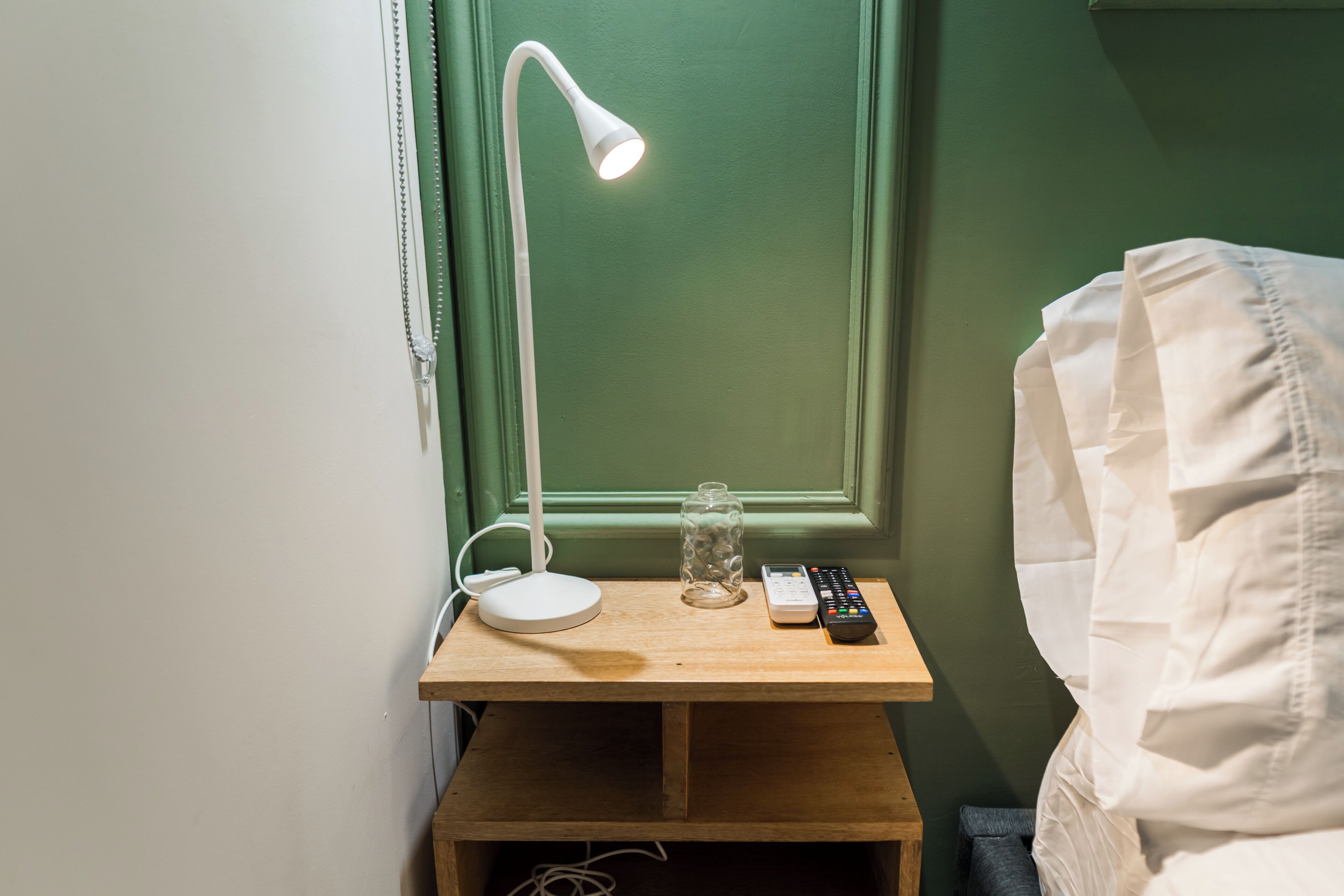 A bedside table with a lamp, a remote control, and a glass jar.