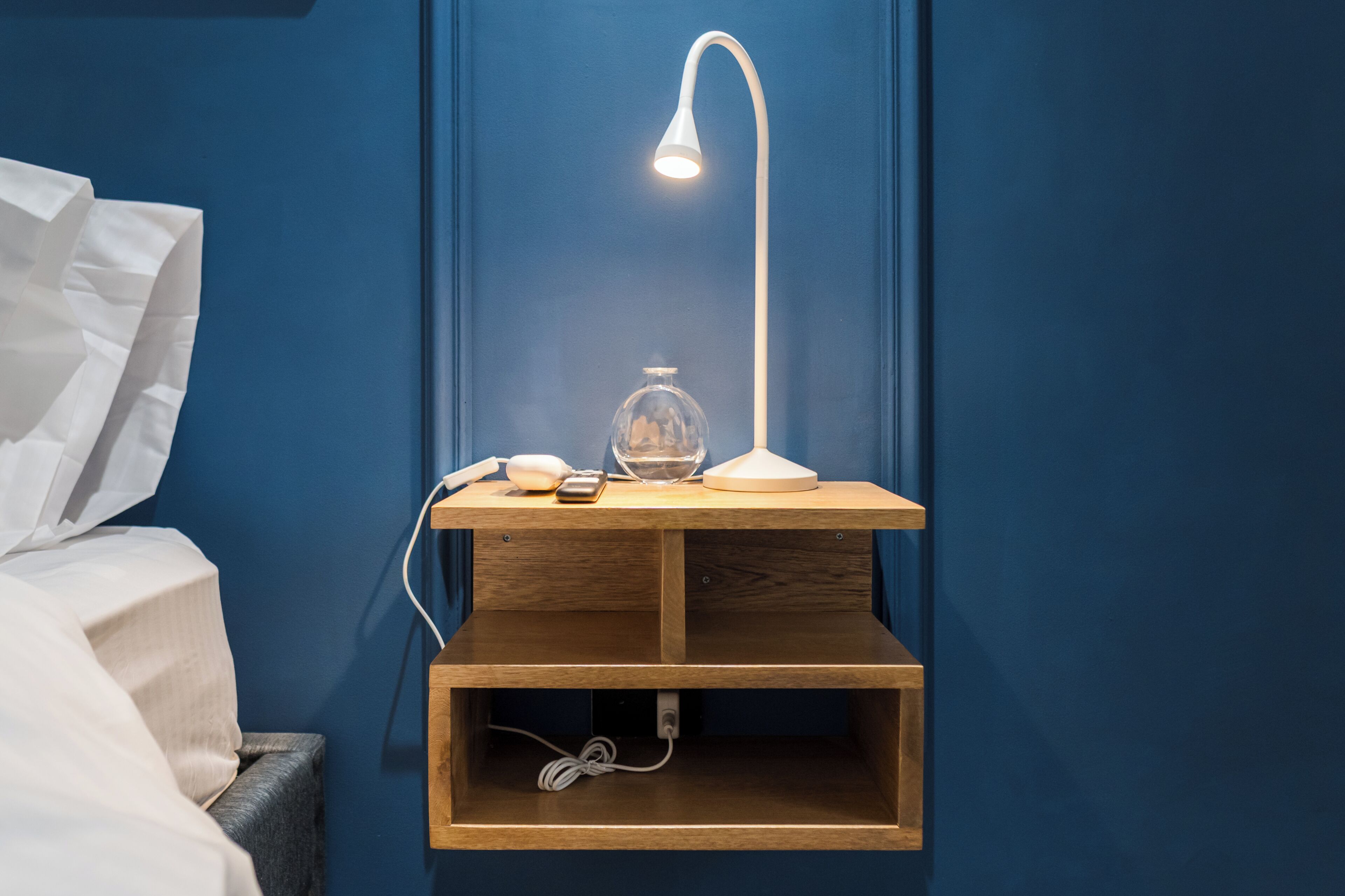 A wooden bedside table with a lamp, a glass bottle, and a smartphone.