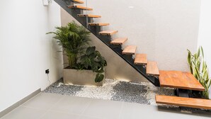 A modern staircase with wooden steps and a glass railing, leading to a landing area with a potted plant and a bench. - Fresco Provenza Living - Musical lifestyle (Medellín)