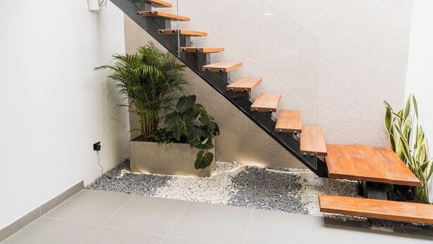 Eine moderne Treppe mit Holzstufen und einem Glasgeländer, die zu einem Landeplatz mit einem Blumentopf und einer Bank führt.