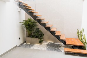 A modern staircase with wooden steps and a glass railing, leading to a landing area with a potted plant and a bench. - Fresco Provenza Living - Musical lifestyle (Medellín)