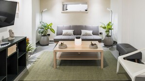 Ein modernes Wohnzimmer mit einem grauen Sofa, einem Couchtisch, einem Fernseher und zwei Blumentöpfen.