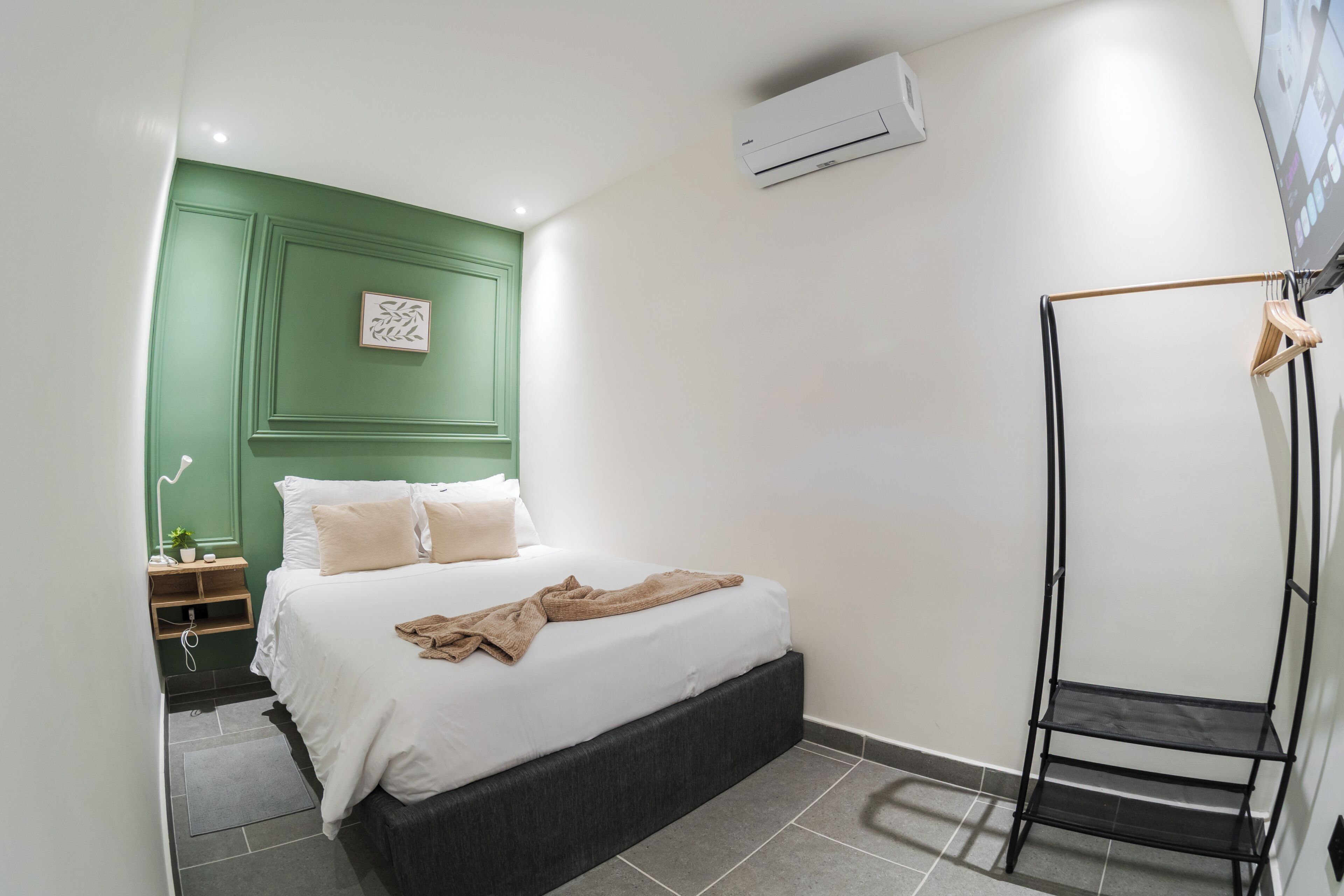 A bedroom with a bed, a bedside table, an air conditioner, and a wall-mounted shelf.