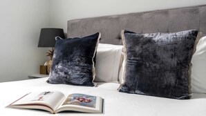 A bed with two dark pillows, a book on it, and a lamp on a bedside table. - The Fox at Hurley - The Warren Suite (Maidenhead)