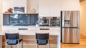 Eine moderne Küche mit einem großen, Edelstahl-Kühlschrank, zwei Backöfen und einem Essbereich mit zwei Stühlen.