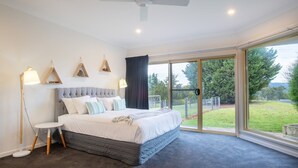 Ein Schlafzimmer mit einem Bett, Nachttischlampen, einem Deckenventilator und einer großen Schiebetür zu einem Garten.