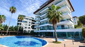 Een modern hotel met een zwembad, palmbomen en een strakblauwe lucht.