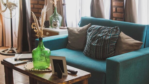 A teal sofa with a picture frame and remote control on a wooden coffee table, a green bottle, and a lamp on a side table.