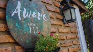 A round sign with 'Aware' and 'LAVALLE 112' on a brick wall, a potted plant, and a lantern.