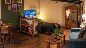 A cozy living room with a television, a wooden cabinet, a bed, and a blue sofa.