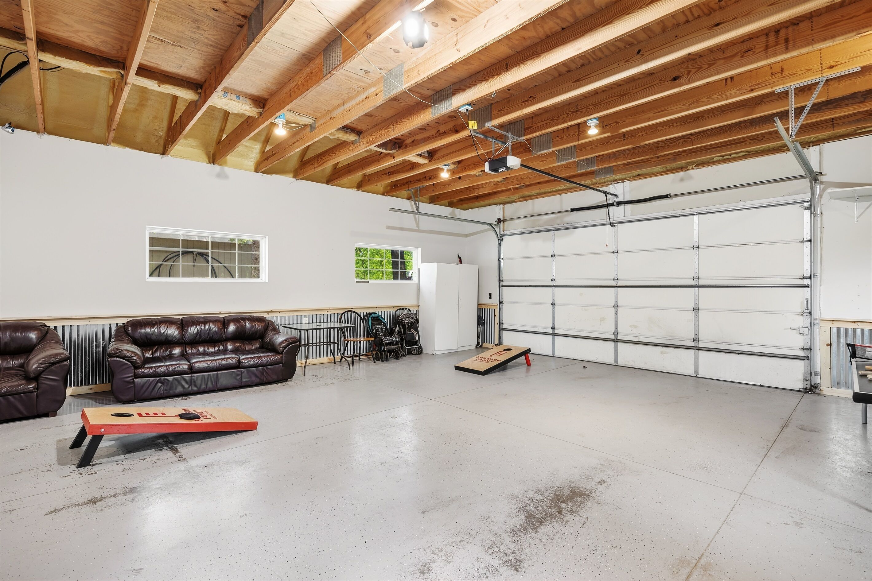 Eine geräumige Garage mit Betonboden, Holzbalken an der Decke, einer weißen Garagentür und einem braunen Ledersofa.