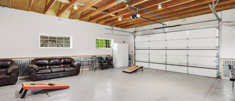 Eine geräumige Garage mit Betonboden, Holzbalken an der Decke, einer weißen Garagentür und einem braunen Ledersofa.