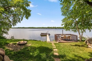 A lakeside deck with a fire pit, outdoor seating, and a dock extending into the water. - Sunset Cabin 4-bedroom cabin in adorable Dassel perfect for relaxing getaways (Dassel)