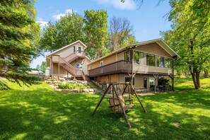 Une maison à deux étages avec une terrasse, une balançoire et un chemin en pierre.