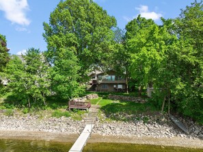 A house with a deck, surrounded by trees and a stone pathway leading to a dock over water. - Sunset Cabin 4-bedroom cabin in adorable Dassel perfect for relaxing getaways (Dassel)