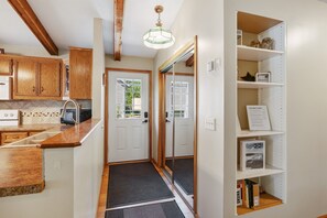 A kitchen with wooden cabinets, a countertop, a toaster, and a door leading to a room with a mirror and shelves. - Sunset Cabin 4-bedroom cabin in adorable Dassel perfect for relaxing getaways (Dassel)