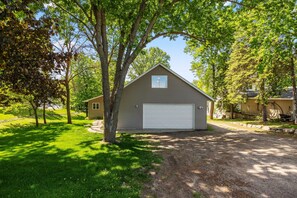 Une maison de plain-pied avec un garage, entourée d’arbres et d’une pelouse bien entretenue.