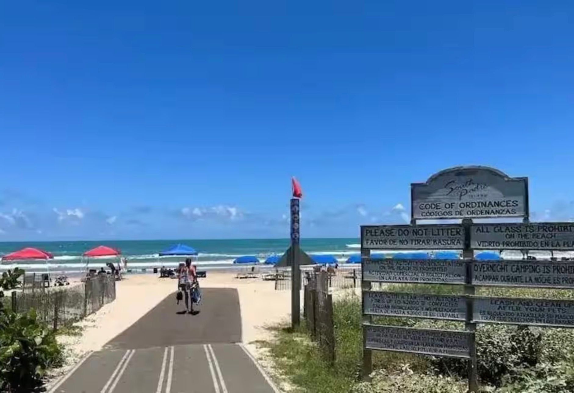 Entrada da praia com uma placa, um caminho e guarda-sóis.