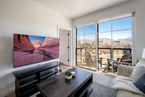 Ein modernes Wohnzimmer mit großem Fernseher, einem Balkon mit Sitzgelegenheit und Blick auf die Berge.